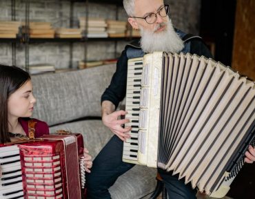 A young girl and her instructor playing accordions during a music lesson indoors.